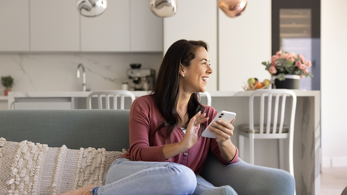 Femme souriante utilisant son smartphone sur un canapé, ambiance chaleureuse et détendue